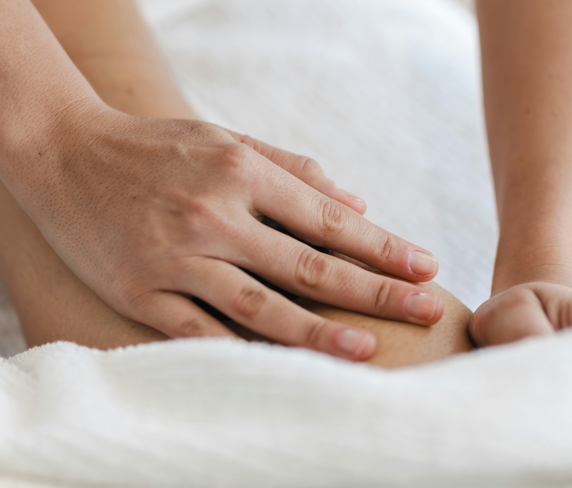 Close up for a hand performing a leg massage with off-white linens.