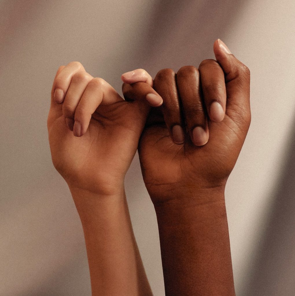 Two hands of different ethnicities holding hands in a "pinky promise" style.