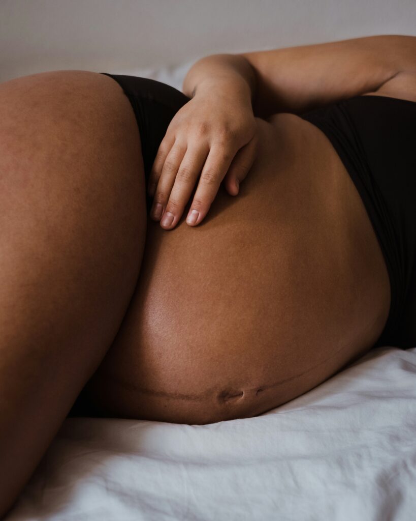 A mid-shot of a pregnant stomach as they lie on their side. The tummy is exposed while they wear a black top and briefs.