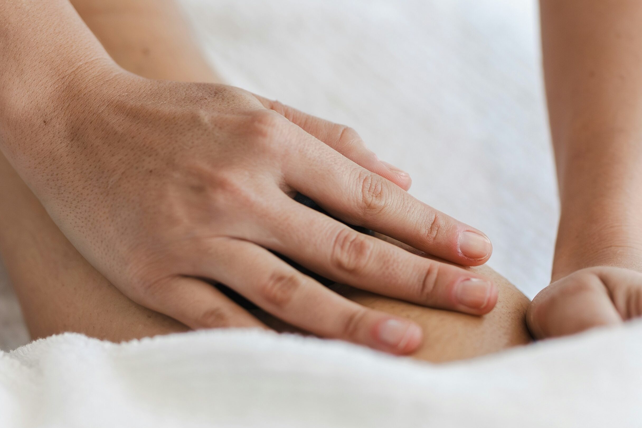 A close up of hands giving someone a massage while surrounded by white towels.