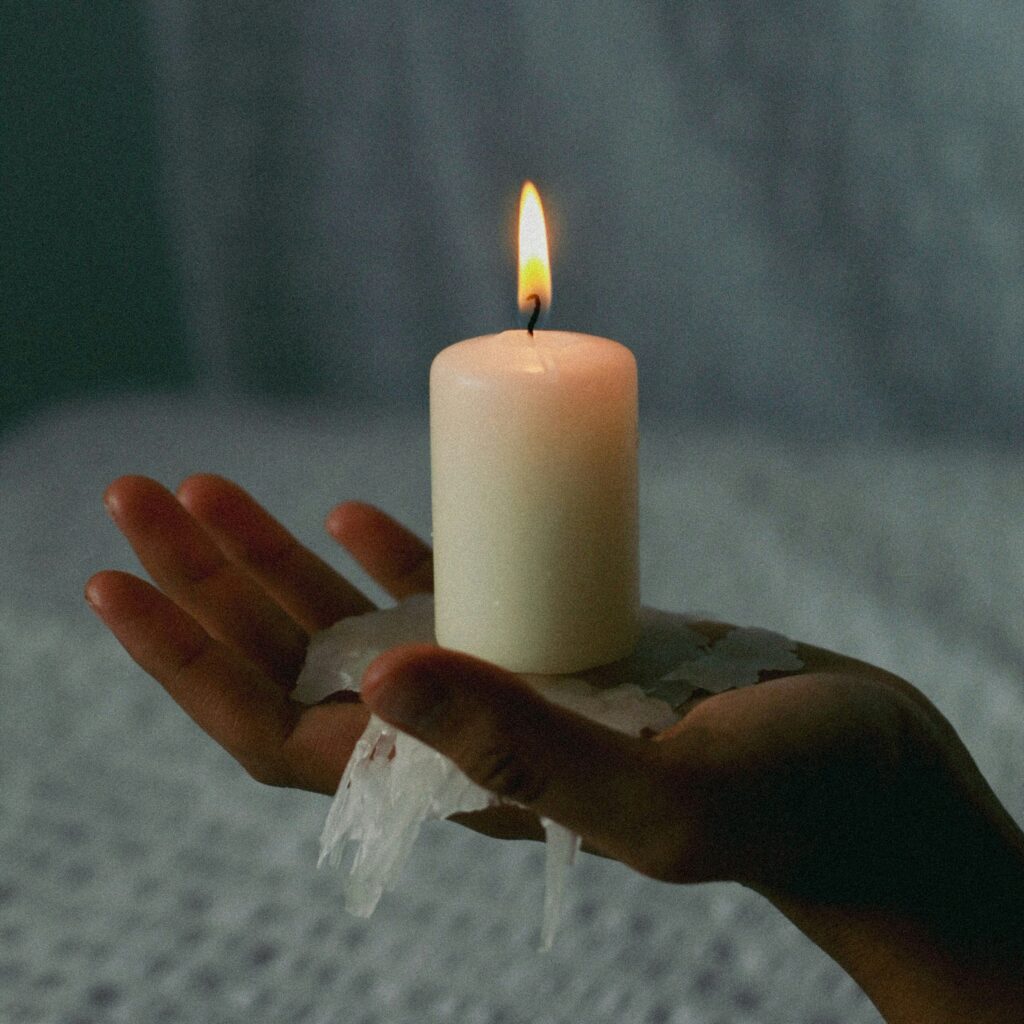 An image of a hand holding a lit pillar candle, the hand has melted wax on it.